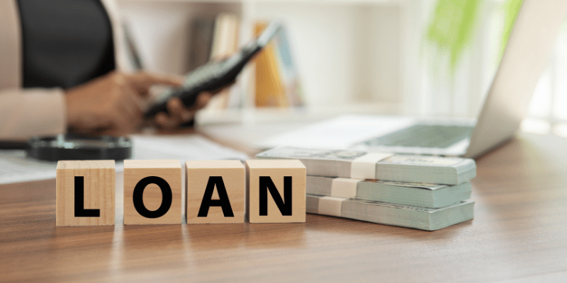 loan spelled on blocks next to cash with woman in the background